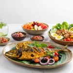 Sajian menu diet Mediterania ala Indonesia di atas meja putih bersih, menampilkan ikan kembung bakar bumbu kuning di atas daun pisang, didampingi mangkuk nasi merah, salad sayur segar dengan tempe dan telur rebus, semangkuk buah potong, aneka sambal tradisional, serta segelas infused water.