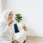 Seorang ibu rumah tangga sedang duduk di dalam rumah dan meminum susu herbal.
